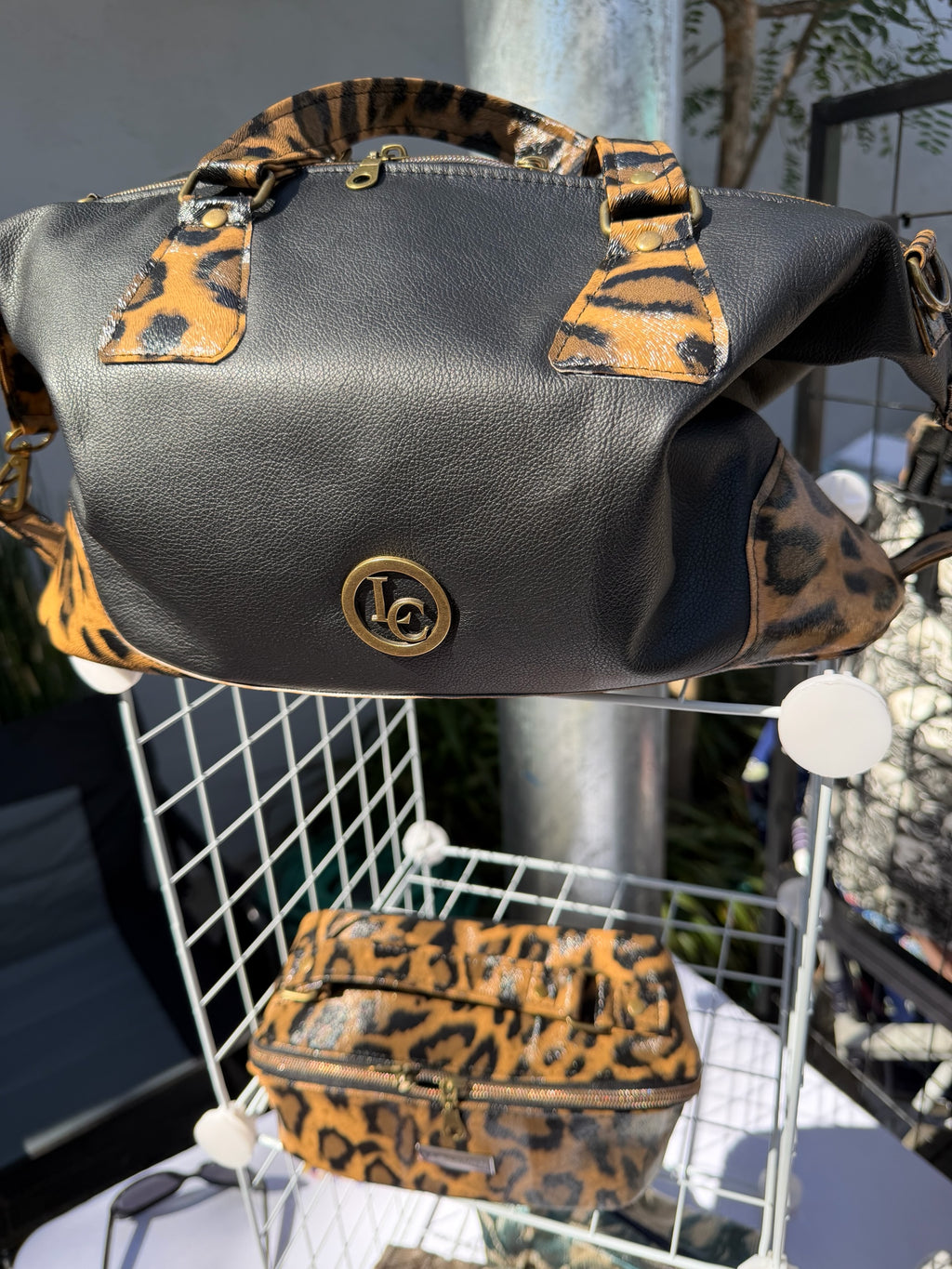 Lacarmenbags black faux leather handbag with leopard print accents, gold-tone logo emblem, and sturdy handles.