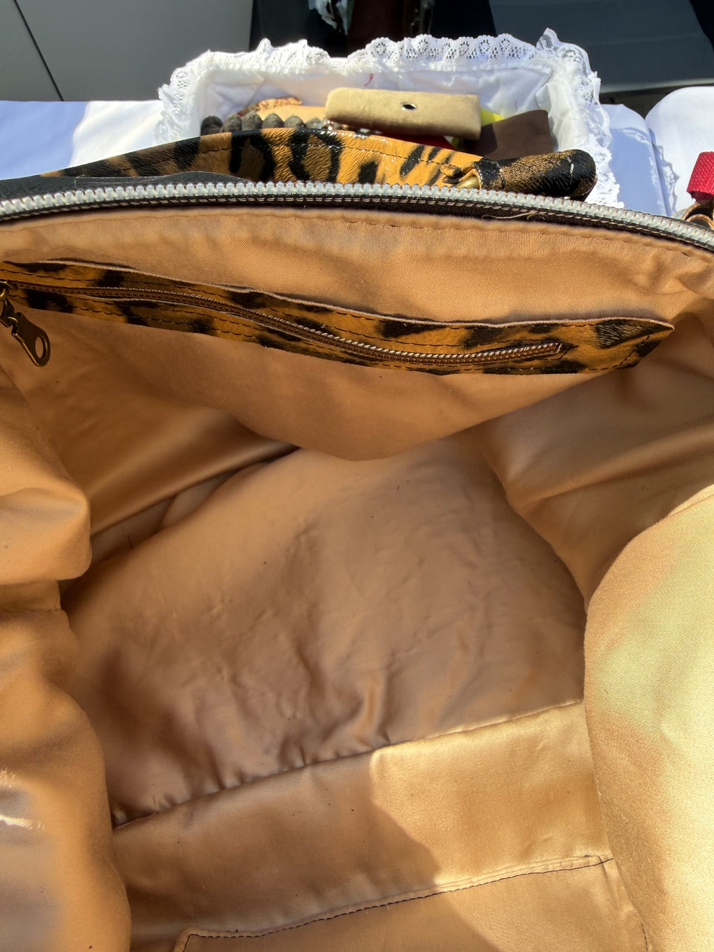 Interior of a Lacarmenbags handbag featuring champagne-colored lining, leopard print trim, and a zippered pocket.
